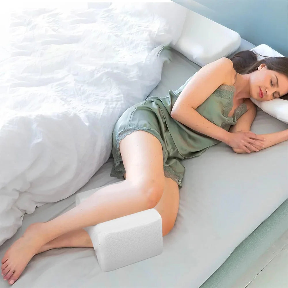 Kvinna sover på sidan med stödjande benkudde i sovrum, ergonomisk sovkudde för avlastning